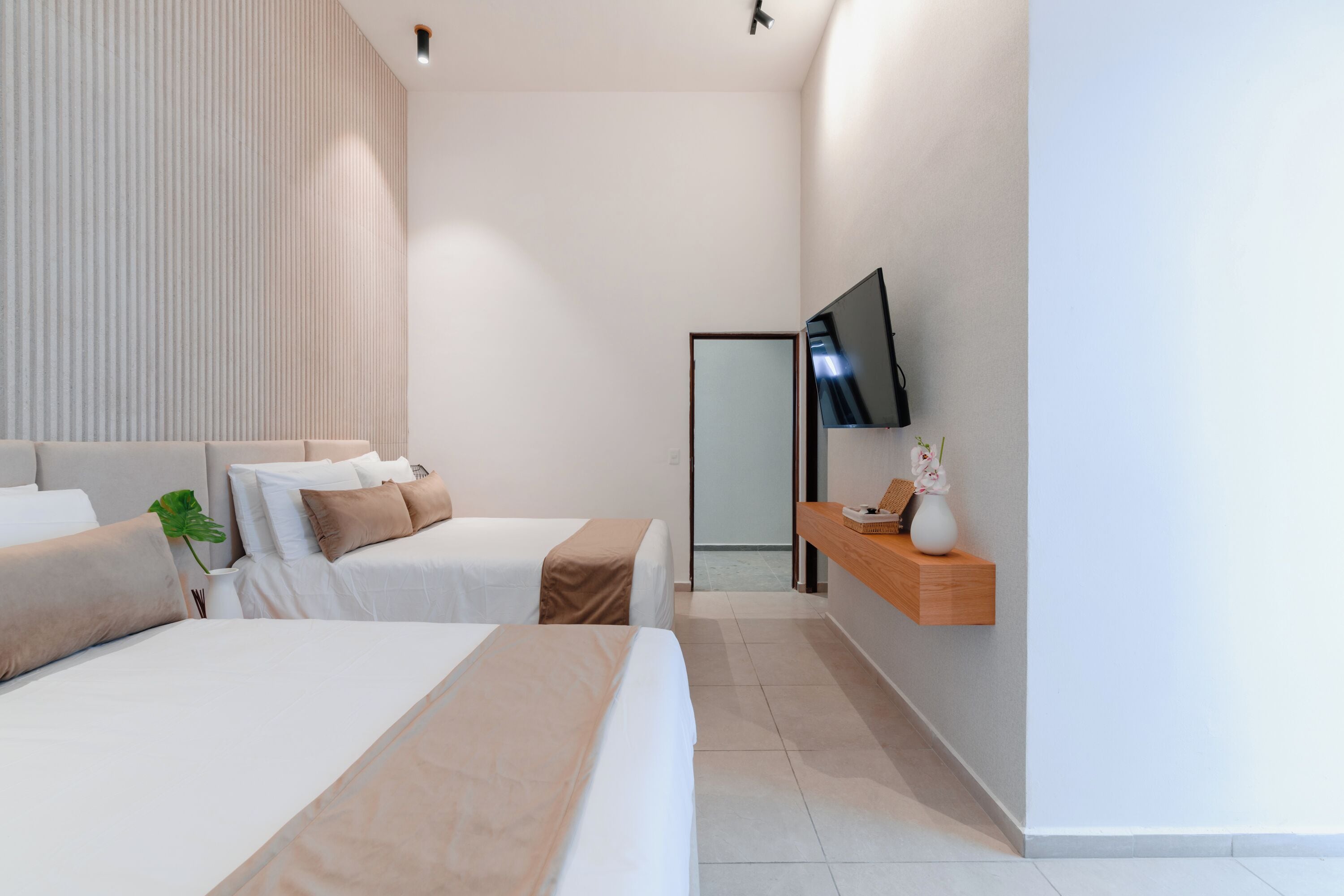 Een moderne hotelkamer met twee bedden, een aan de muur bevestigde televisie en een klein houten plankje met een vaas.