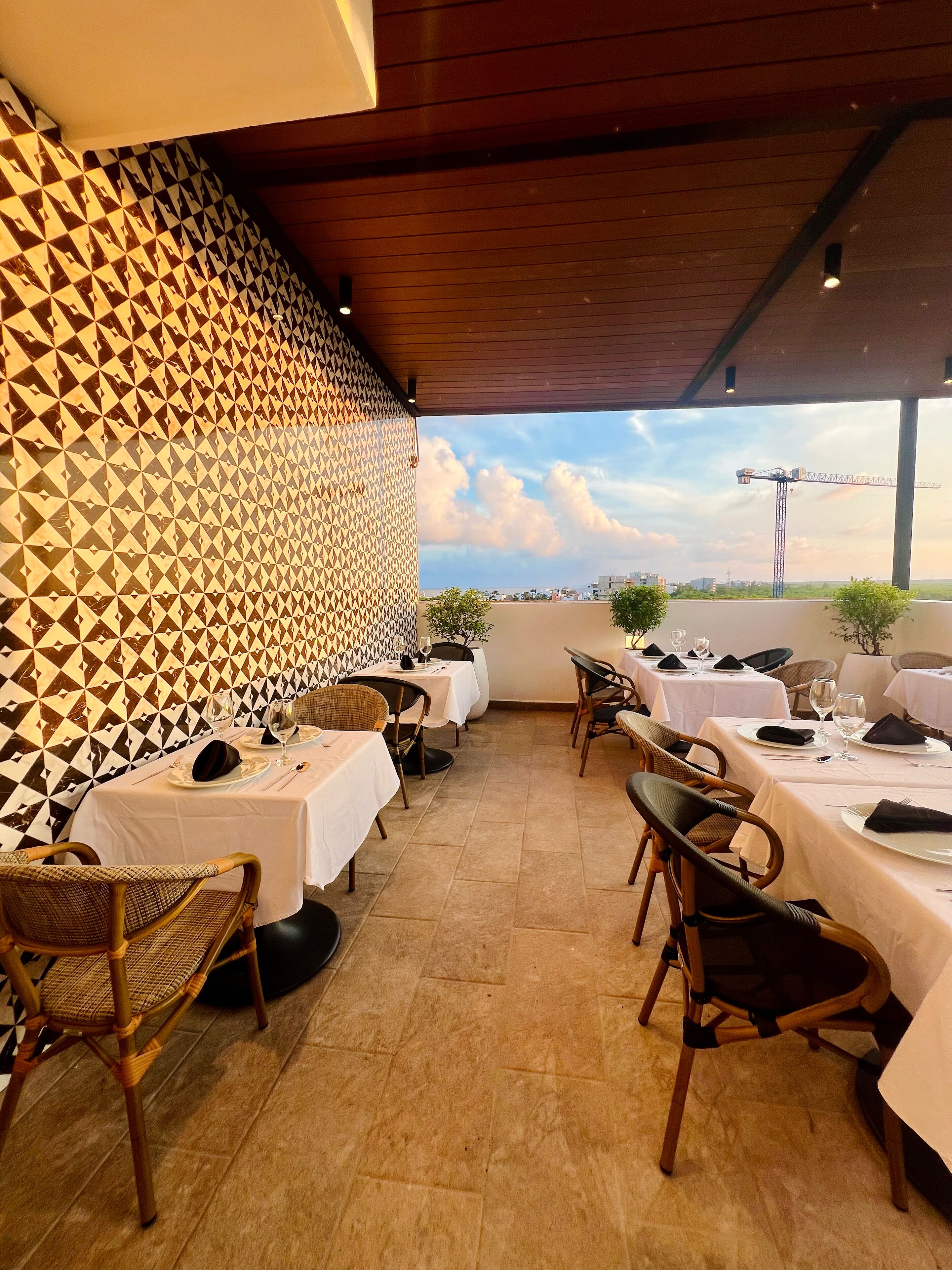 An outdoor dining area with tables set for two, a patterned wall, and a view of the city skyline.