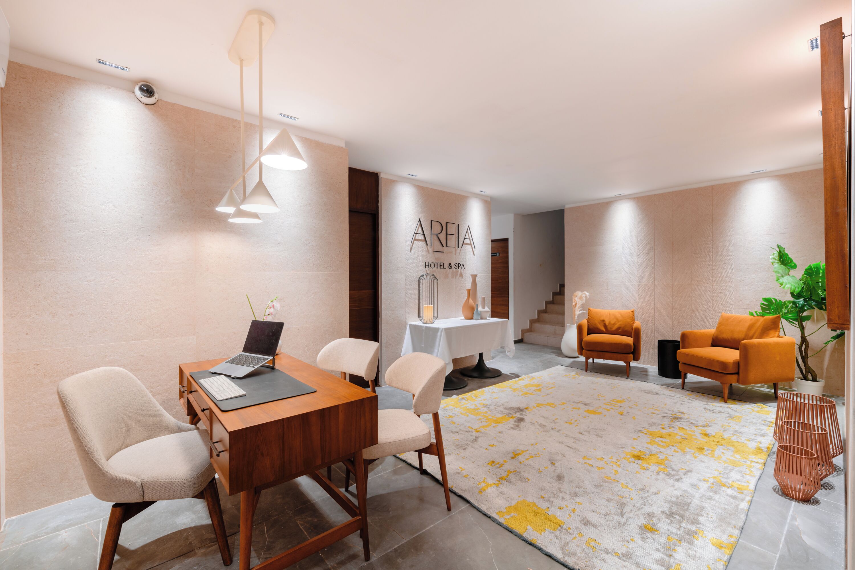 Un vestíbul d'hotel modern amb una taulell de recepció de fusta, cadires beix, un moqueta estampada en groc i gris, i butaques taronges.