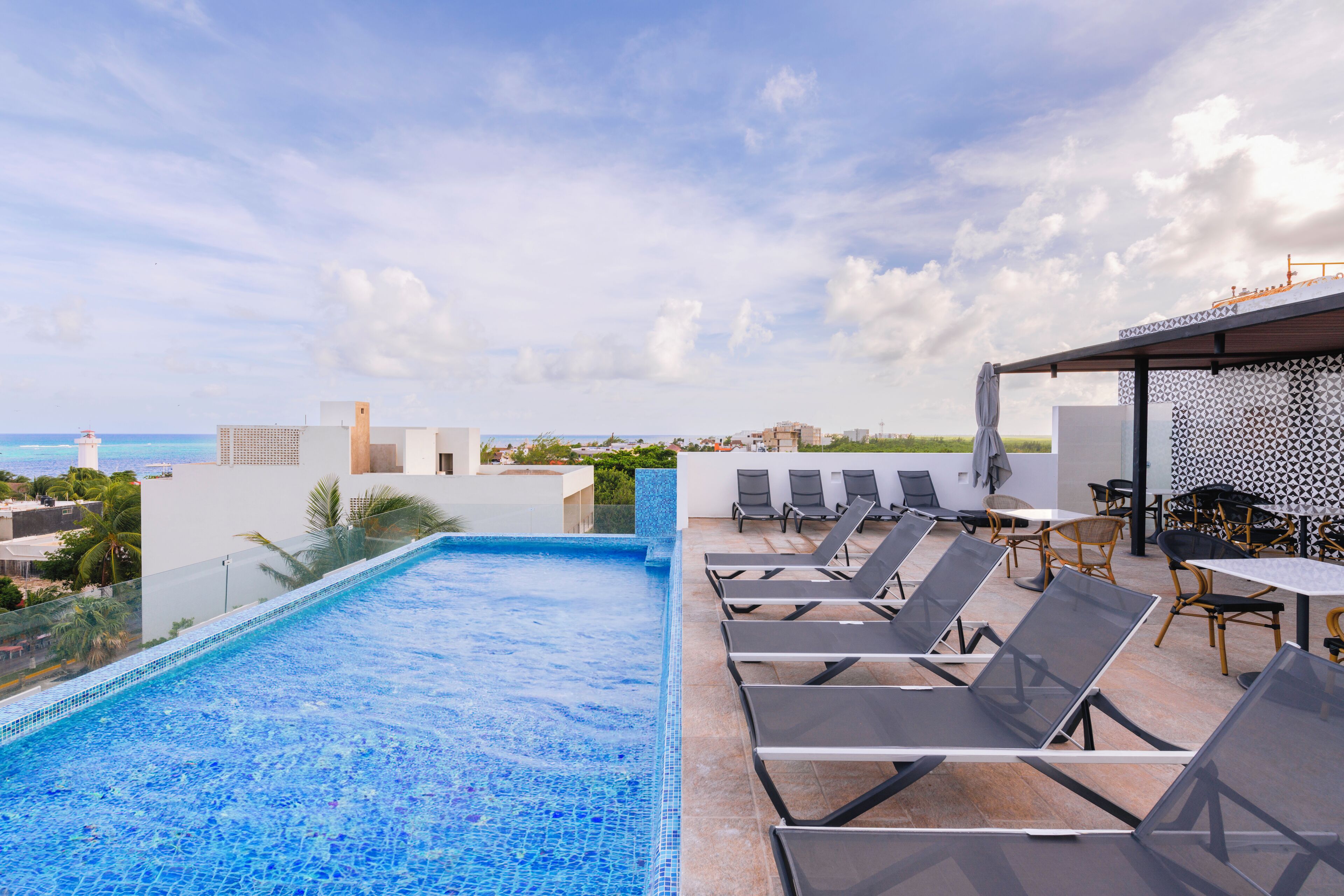 A rooftop pool with lounge chairs and a dining area overlooking the ocean.