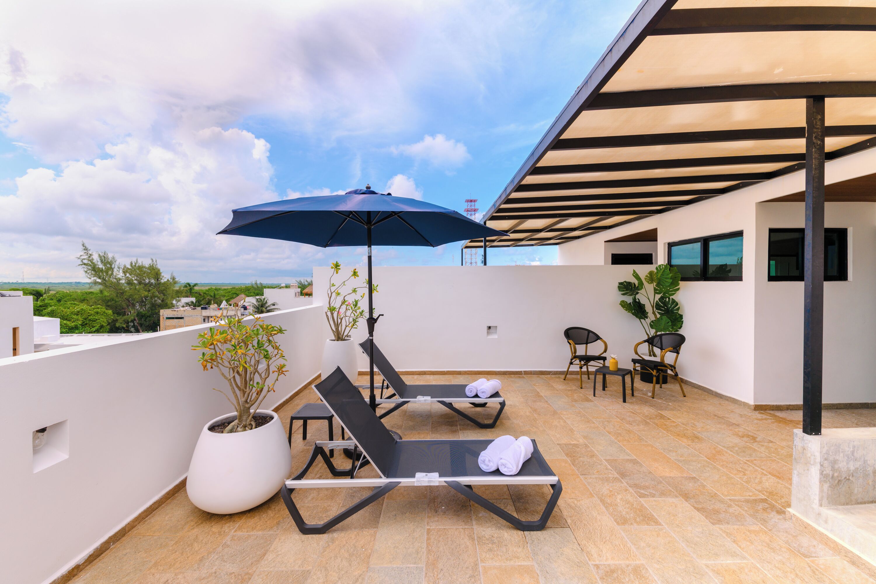 Terraço no telhado com duas cadeiras de descanso, uma planta em vaso, uma mesa e um guarda-sol.