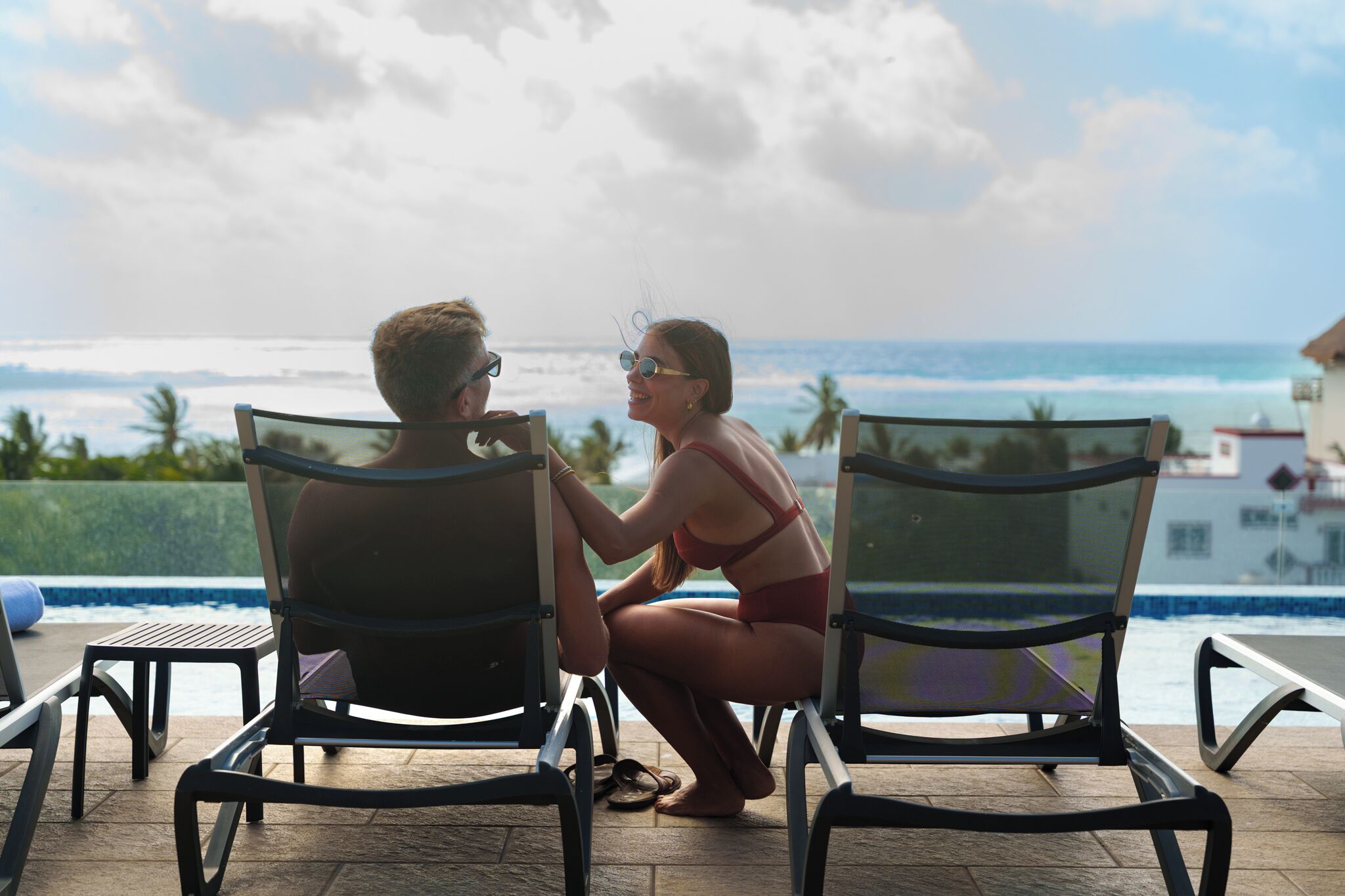 Dos personas sentadas en sillones frente a una piscina con vista al océano.