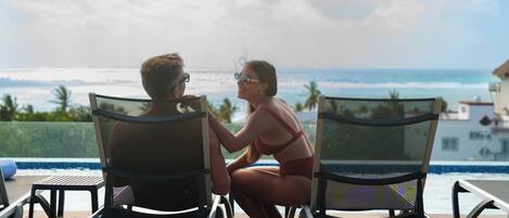 Dos personas sentadas en sillones frente a una piscina con vista al océano.