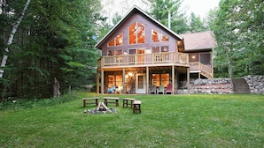 A cabin with a porch, outdoor seating, and a stone wall. - Lakefront Cabin w/ Pool Table+Waterfall: Northwoods Nostalgia + Modern Amenities (Clam Lake)