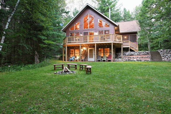 A cabin with a porch, outdoor seating, and a stone wall. - Lakefront Cabin w/ Pool Table+Waterfall: Northwoods Nostalgia + Modern Amenities (Clam Lake)