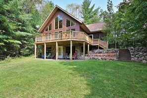 A two-story cabin with a balcony, stone foundation, and a stone wall. - Lakefront Cabin w/ Pool Table+Waterfall: Northwoods Nostalgia + Modern Amenities (Clam Lake)
