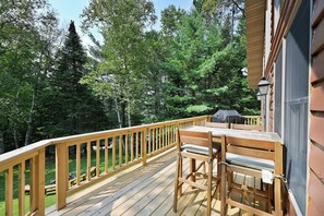 A wooden deck with a table and chairs, surrounded by trees. - Lakefront Cabin w/ Pool Table+Waterfall: Northwoods Nostalgia + Modern Amenities (Clam Lake)
