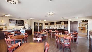 Un comedor de hotel con varias mesas y sillas de madera, una zona de bar y una cocina al fondo.