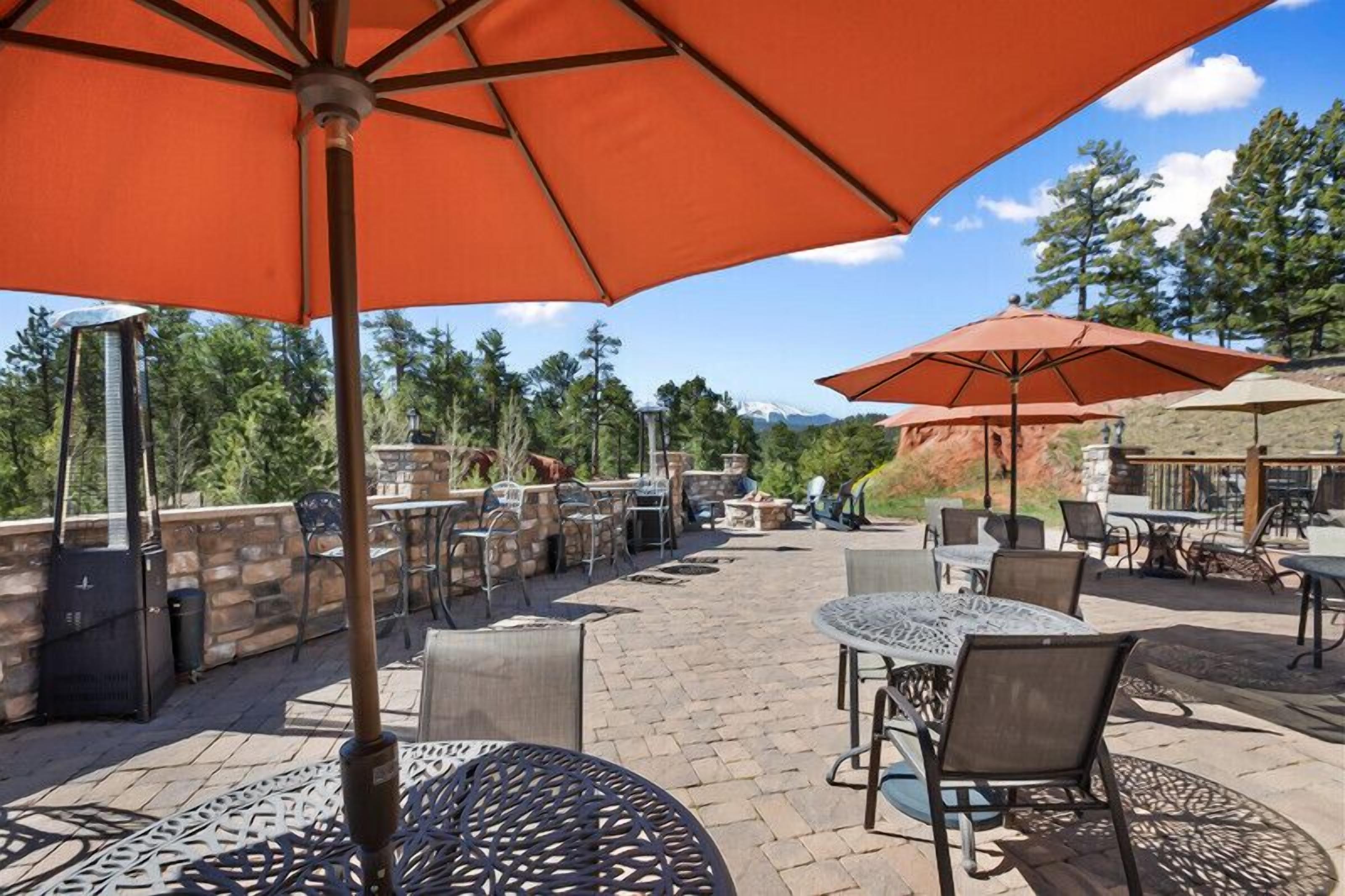 An outdoor patio with tables and chairs, umbrellas, and a stone wall.
