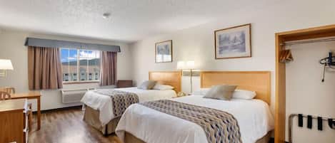 A hotel room with two beds, a desk, a chair, a window with curtains, and a coat rack.