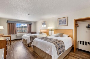Habitación de hotel con dos camas, un escritorio, una silla, un ventanal con cortinas y un perchero.