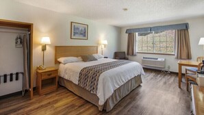 Ett hotellrum med en säng, sängbord, ett skrivbord, en stol, ett fönster med gardiner och ett element.