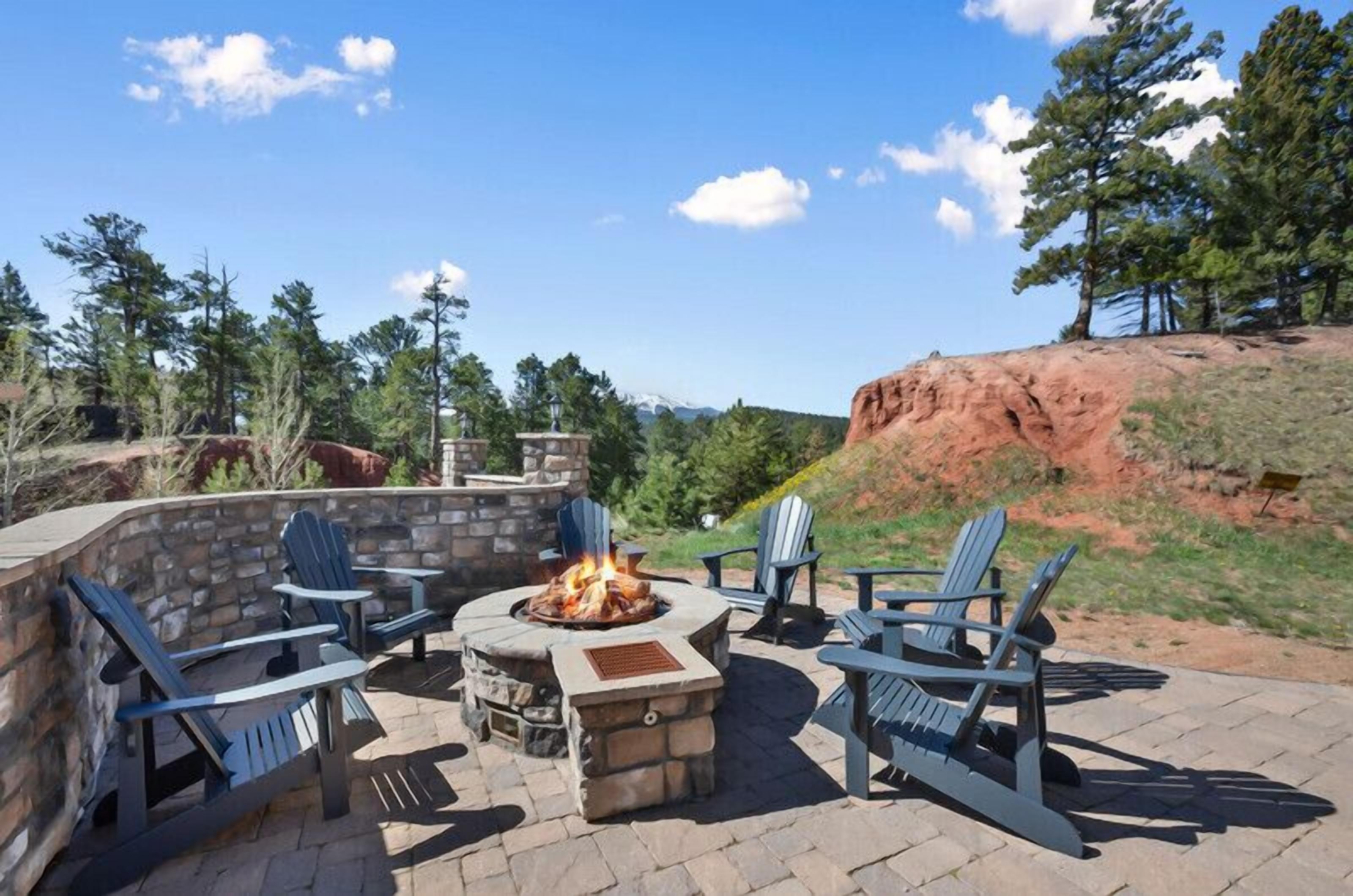 Une terrasse extérieure avec des fauteuils Adirondack, un foyer en pierre et un mur en pierre.