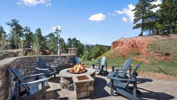 An outdoor patio with Adirondack chairs, a stone fire pit, and a stone wall.