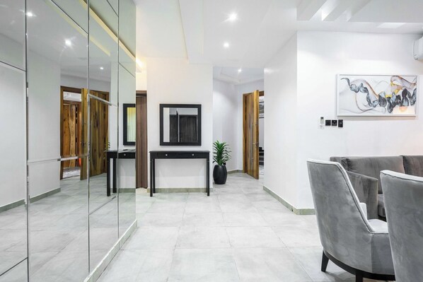 A modern lobby with a glass wall, a reception desk, a potted plant, and a grey sofa. - The Azaria Hotel & Apartments (Lekki)