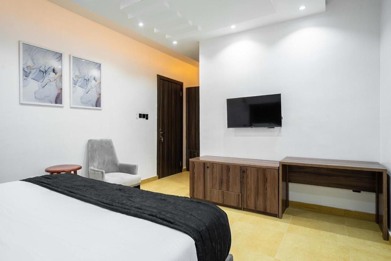 A modern bedroom with a bed, a desk, a chair, a TV, and artwork on the wall.
