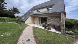 Ein Haus mit schrägem Dach, Steinaußenwand und überdachter Terrasse mit Gartenmöbeln.