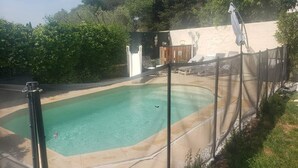 Ein Garten mit Swimmingpool, einer Holzterrasse und einem umzäunten Bereich mit Liegestühlen.