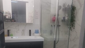 Ein Badezimmer mit Duschkabine aus Glas, einem weißen Waschbecken mit Spiegel darüber und einem gefliesten Boden.