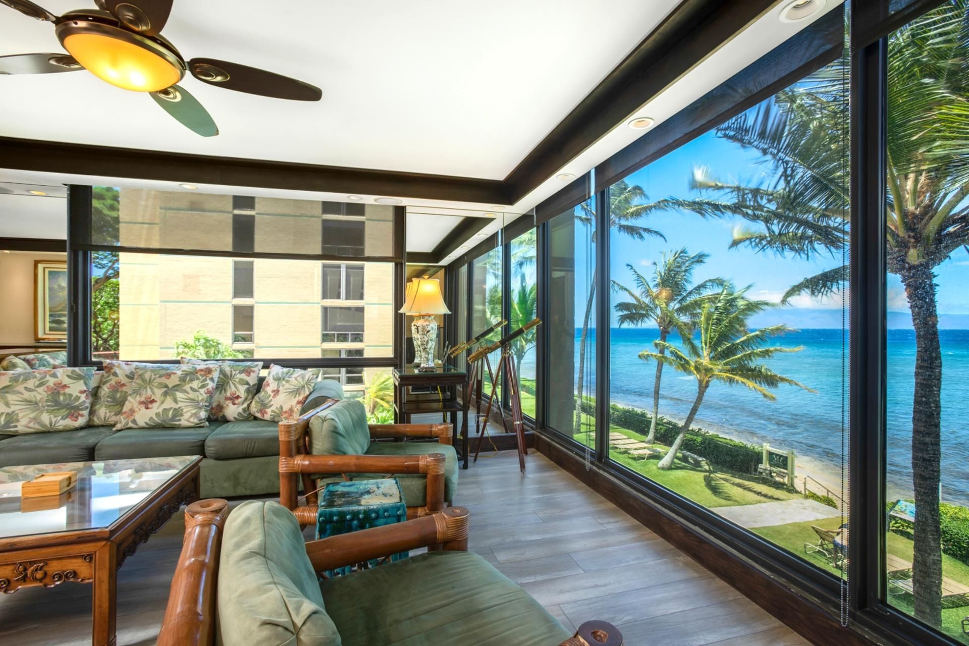 A spacious living area with a large window overlooking a beach, furnished with a sofa, chairs, and a coffee table.