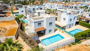 Ett bostadsområde med moderna, vita byggnader, en swimmingpool och utsikt över det omgivande landskapet.