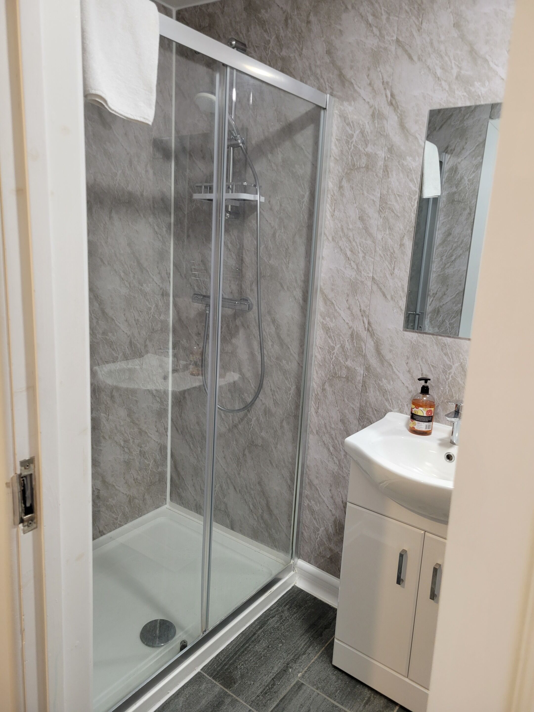 A bathroom with a glass-enclosed shower, a white sink with a soap dispenser, and a cabinet with handles.