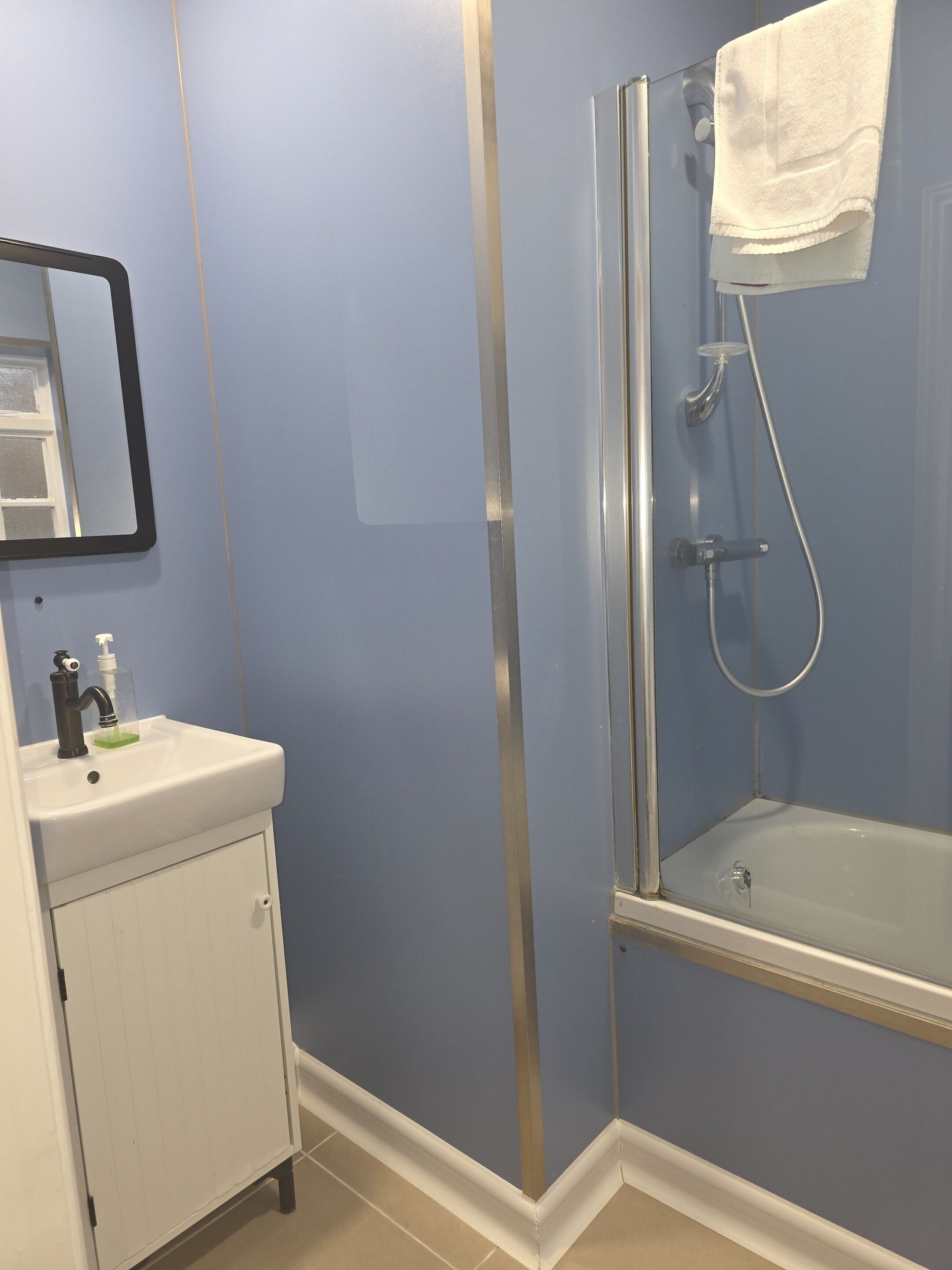 A bathroom with a white sink, a mirror, a glass shower enclosure, and a towel hanging on the shower door.