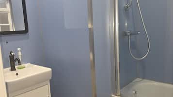 A bathroom with a white sink, a mirror, a glass shower enclosure, and a towel hanging on the shower door.