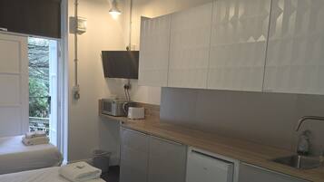 A compact hotel room with a bed, a small kitchenette, a sink, and a chair.