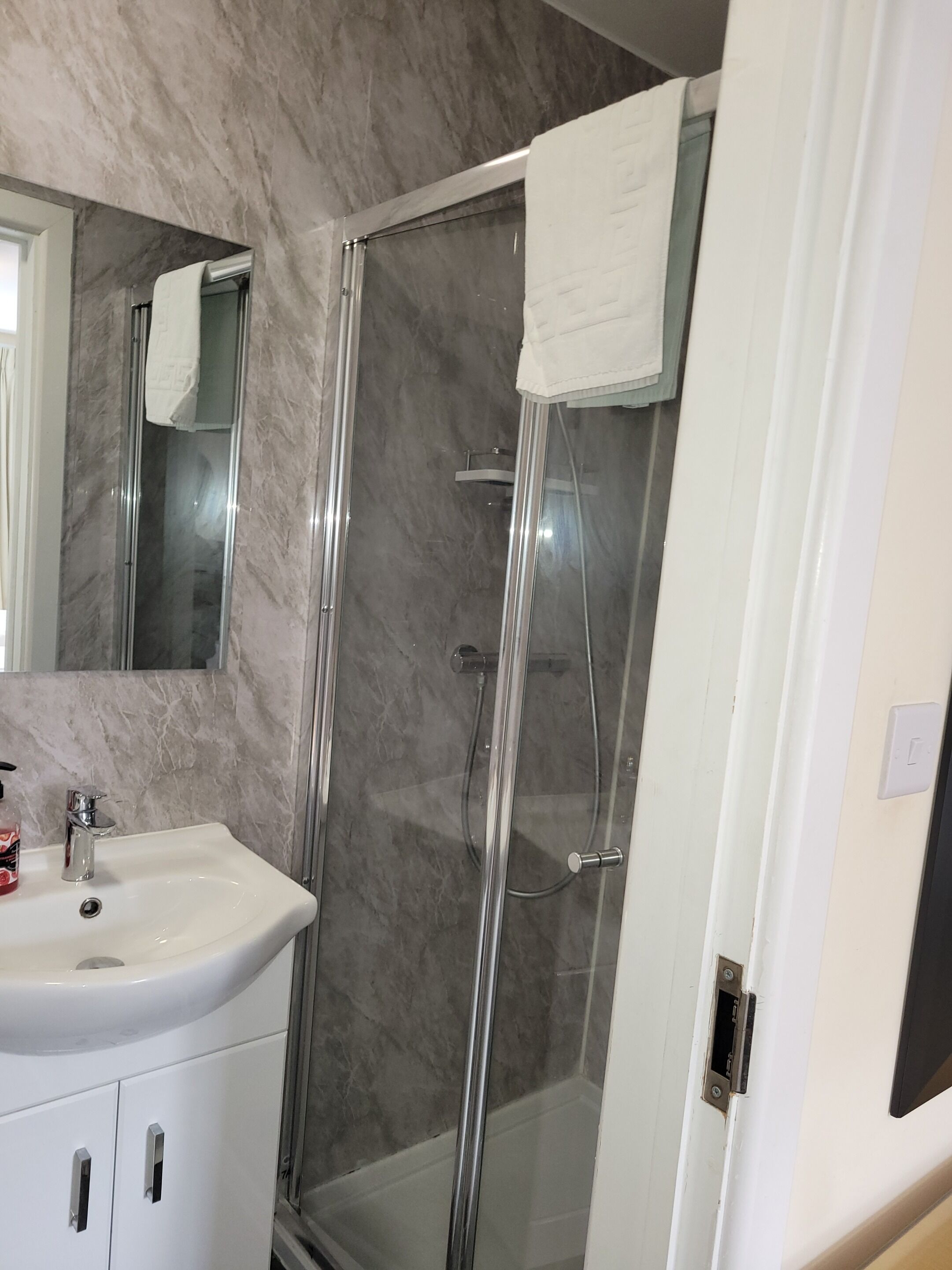 Un baño moderno con ducha de vidrio, lavamanos blanco y salpicadero de mármol.