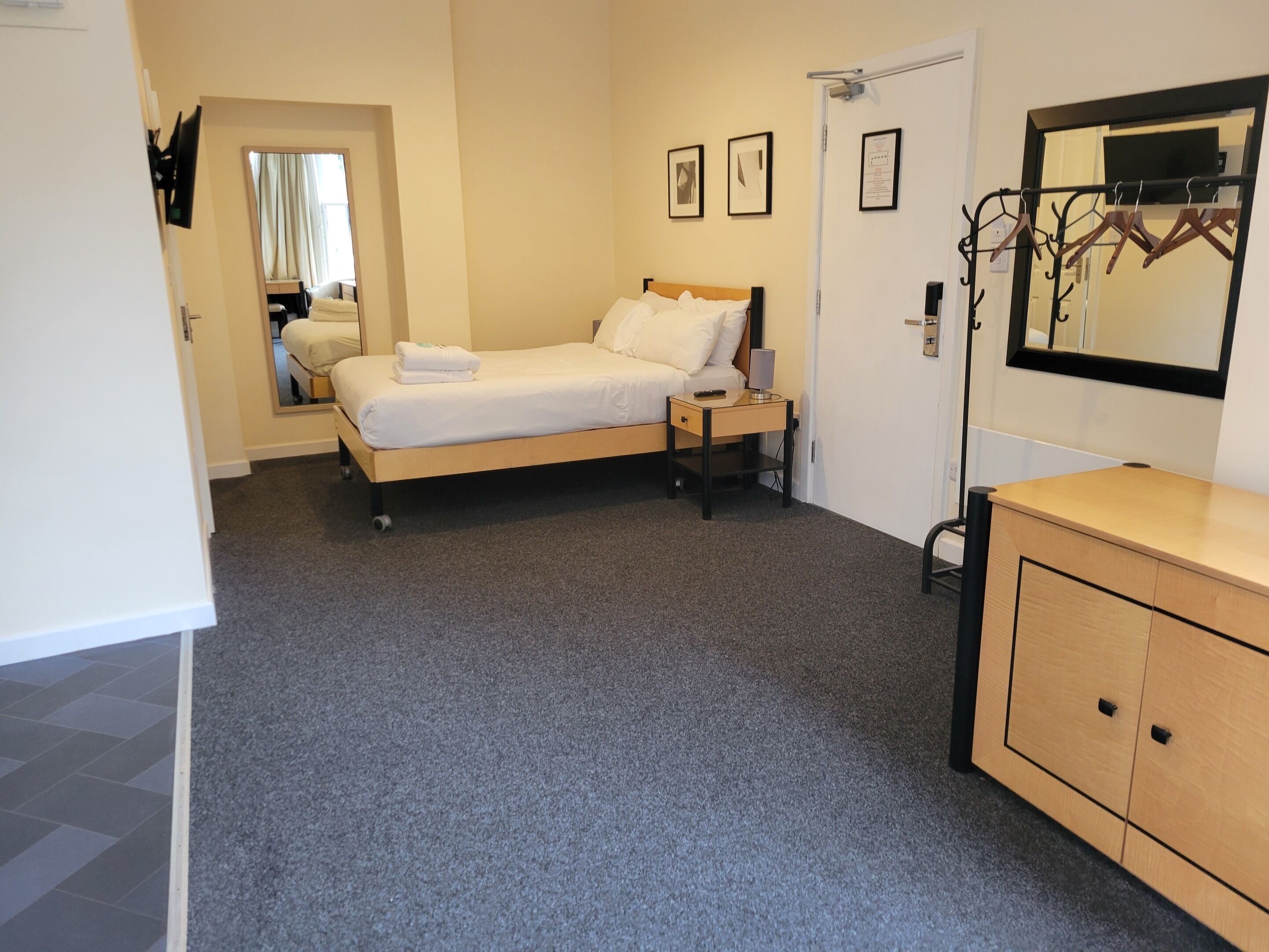 A neatly arranged bedroom with a bed, bedside table, dresser, and a mirror.