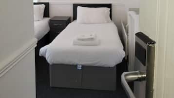 A small, neatly arranged hotel room with a single bed, a bedside table, and a hanging light fixture.