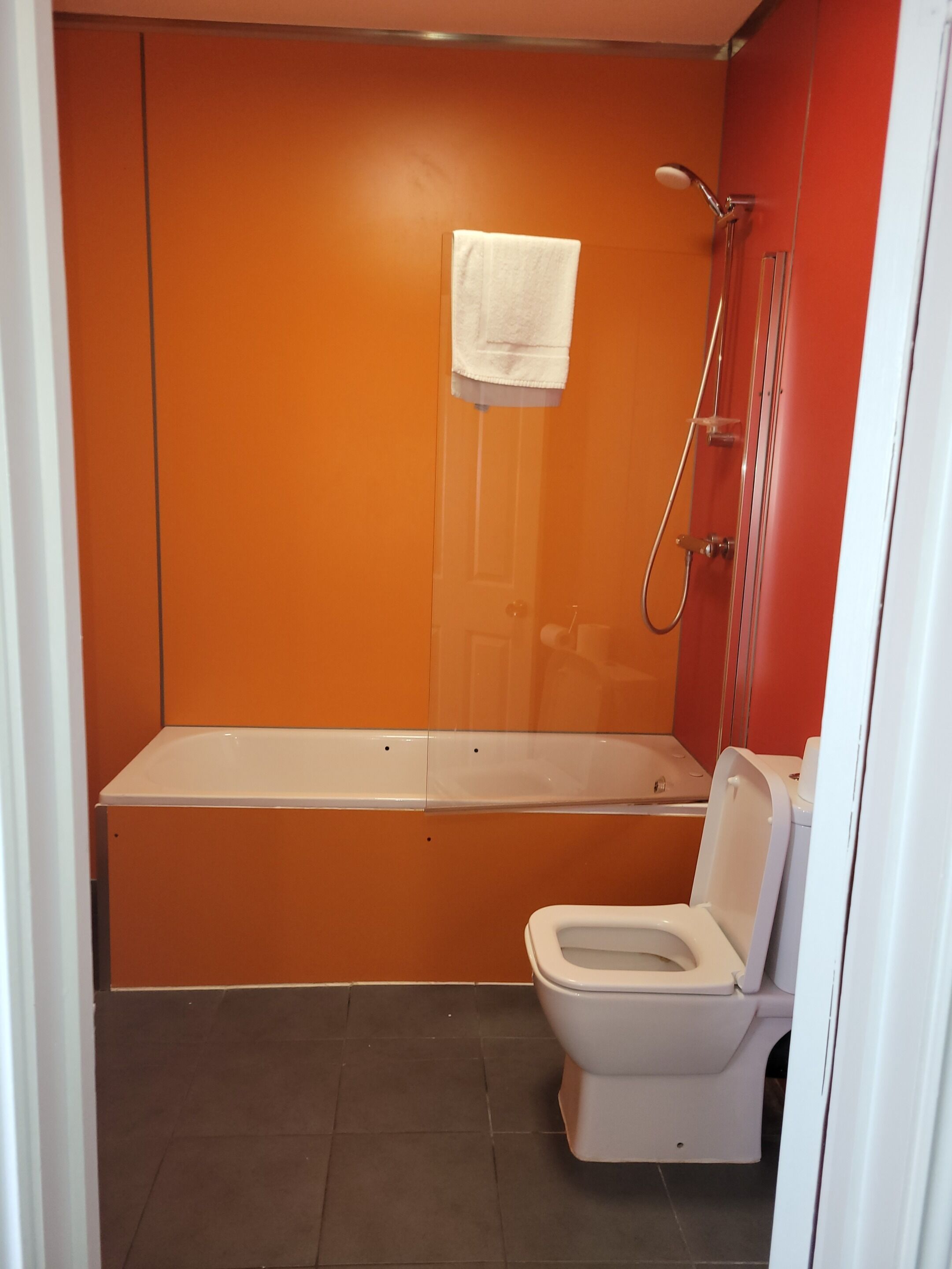 Ein Badezimmer mit orangefarbener Wand, einer weißen Badewanne und einer weißen Toilette.