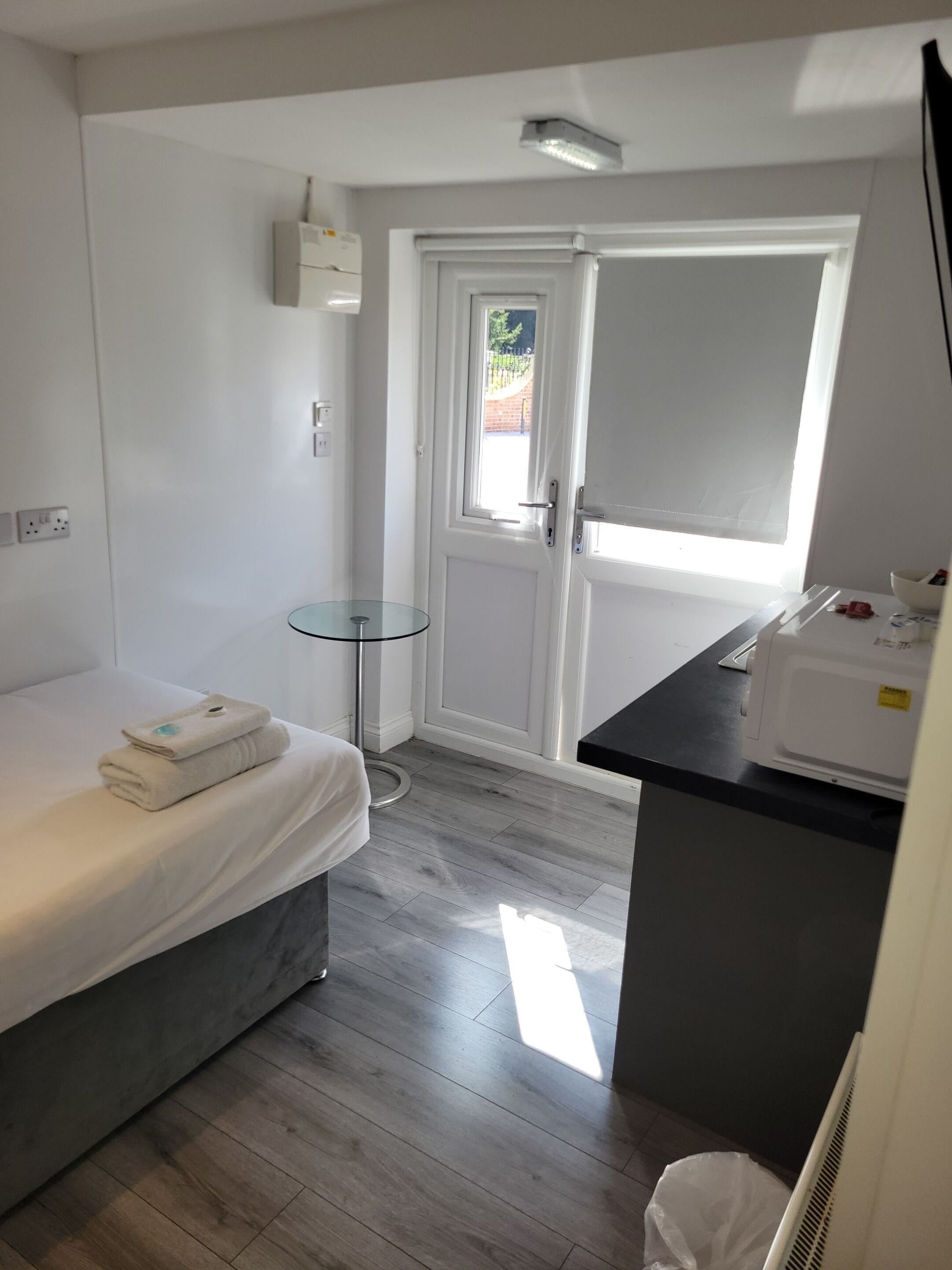 A small, modern room with a bed, a small table, a microwave, and a door leading outside.