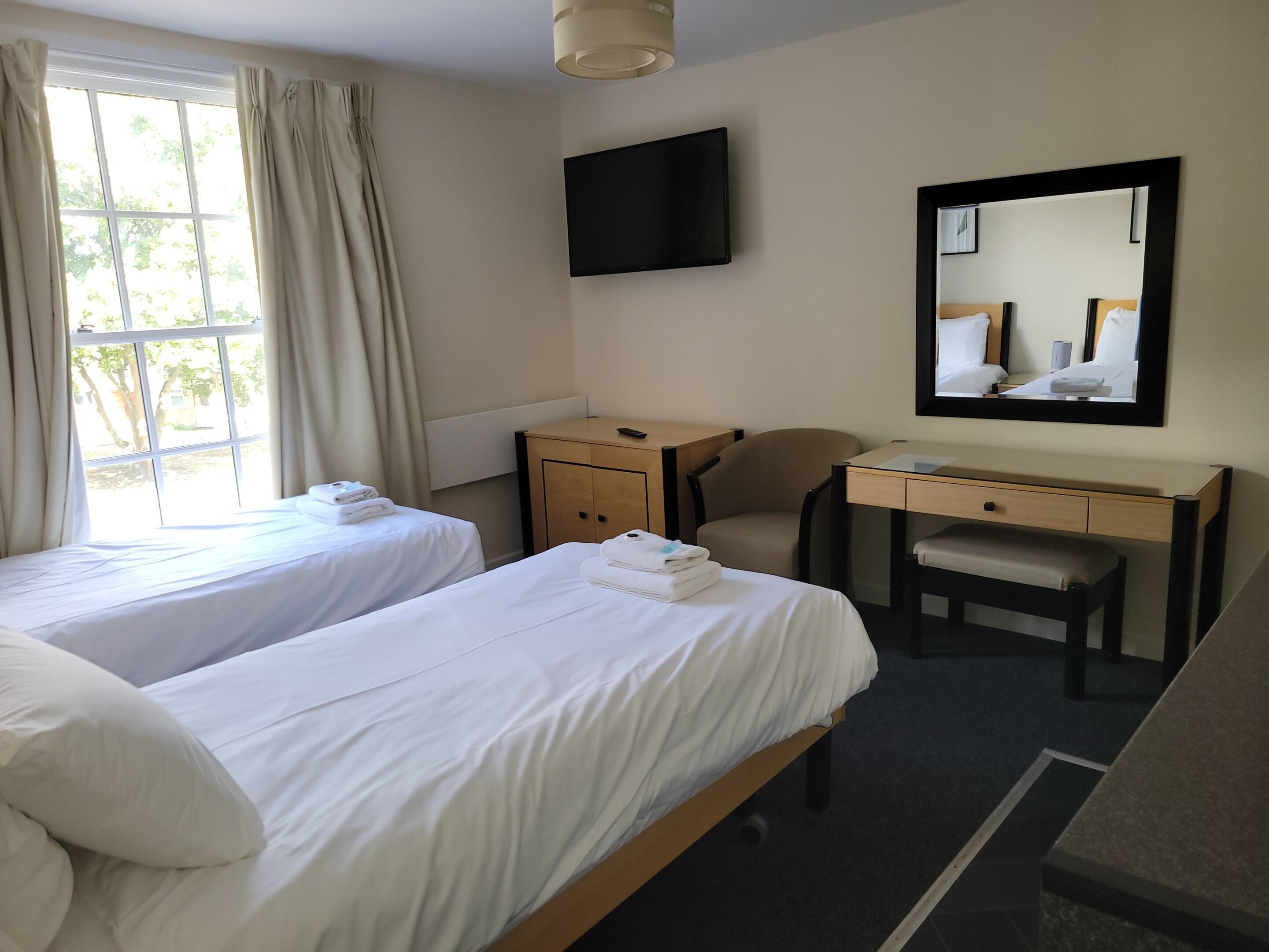 A hotel room with two beds, a desk, a chair, a TV, and a mirror.