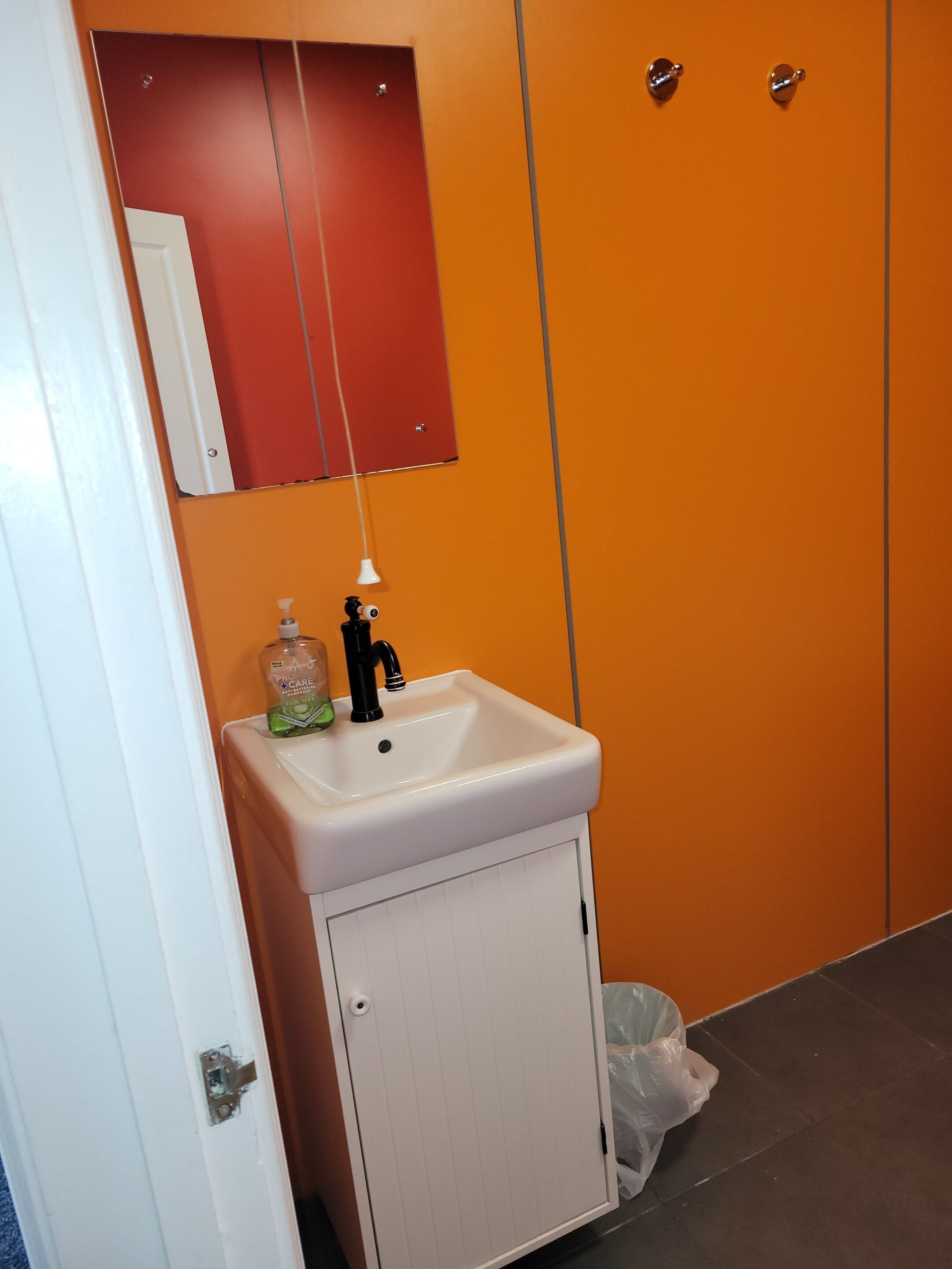 A bathroom with a white sink, a mirror, and an orange wall.