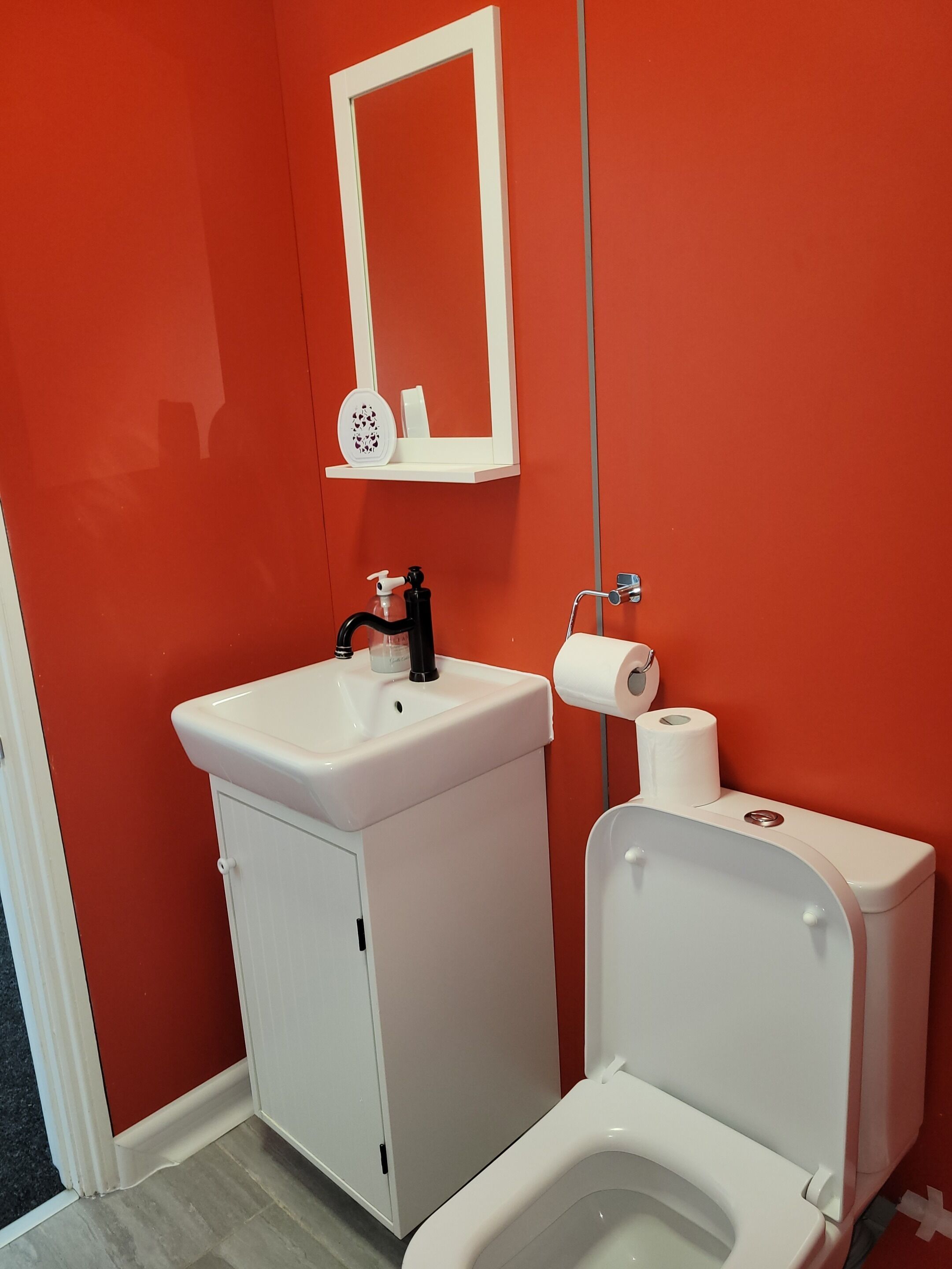 Un baño con un lavamanos blanco, grifo negro y un inodoro con un rollo de papel higiénico.