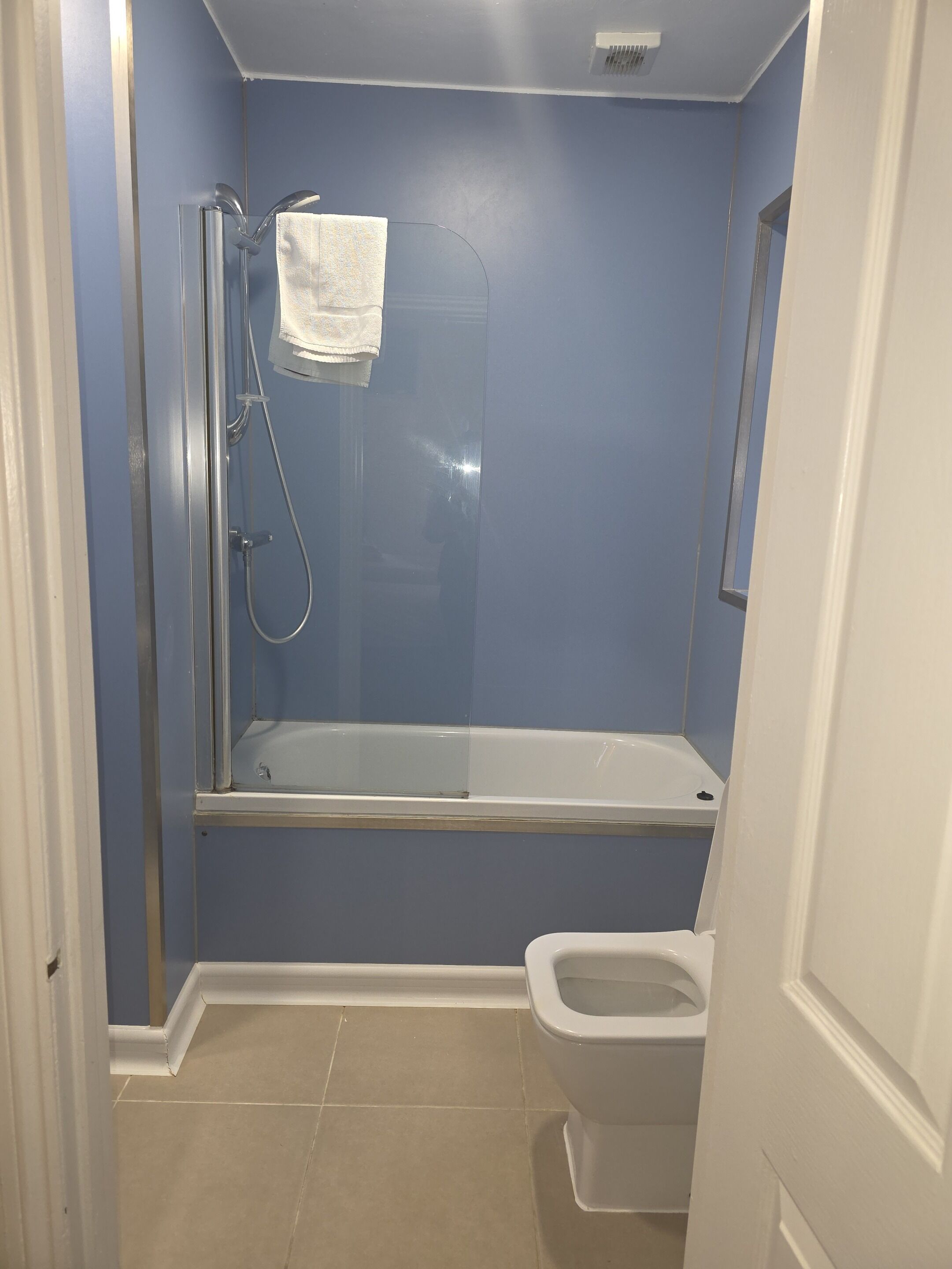 A bathroom with a glass-enclosed shower, a white toilet, and a towel hanging on the wall.