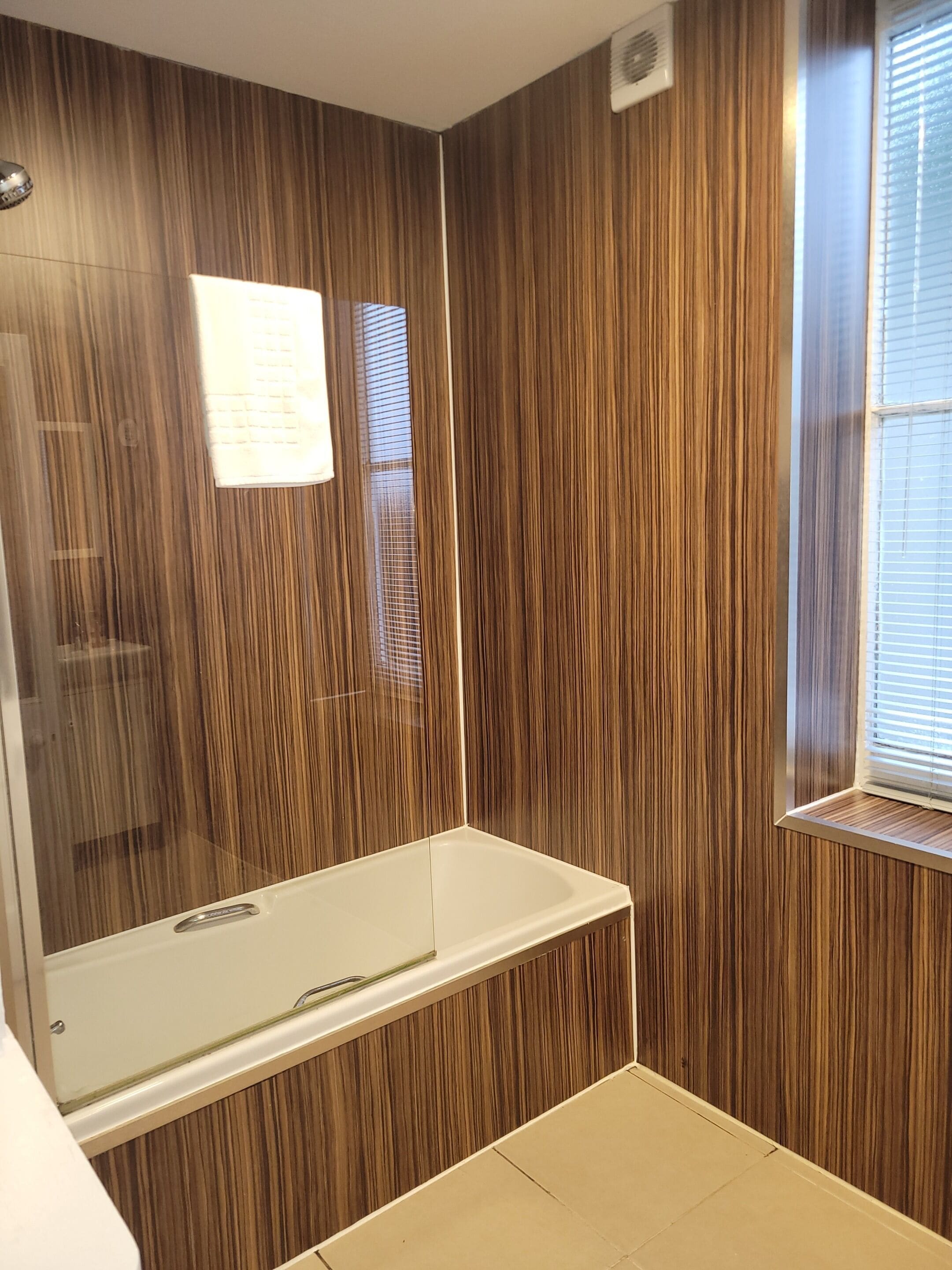 A modern bathroom with a wooden panel wall, a glass-enclosed shower, and a window with blinds.