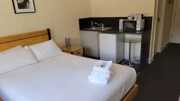 A hotel room with a bed, a small kitchenette, a refrigerator, and a glass table.
