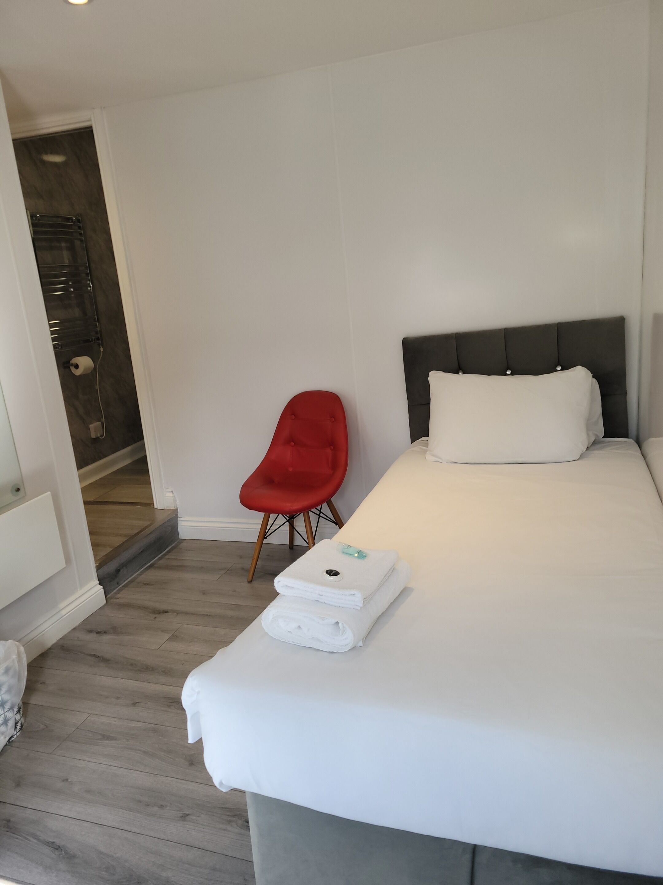 A hotel room with a bed, a red chair, and a bathroom visible through an open door.
