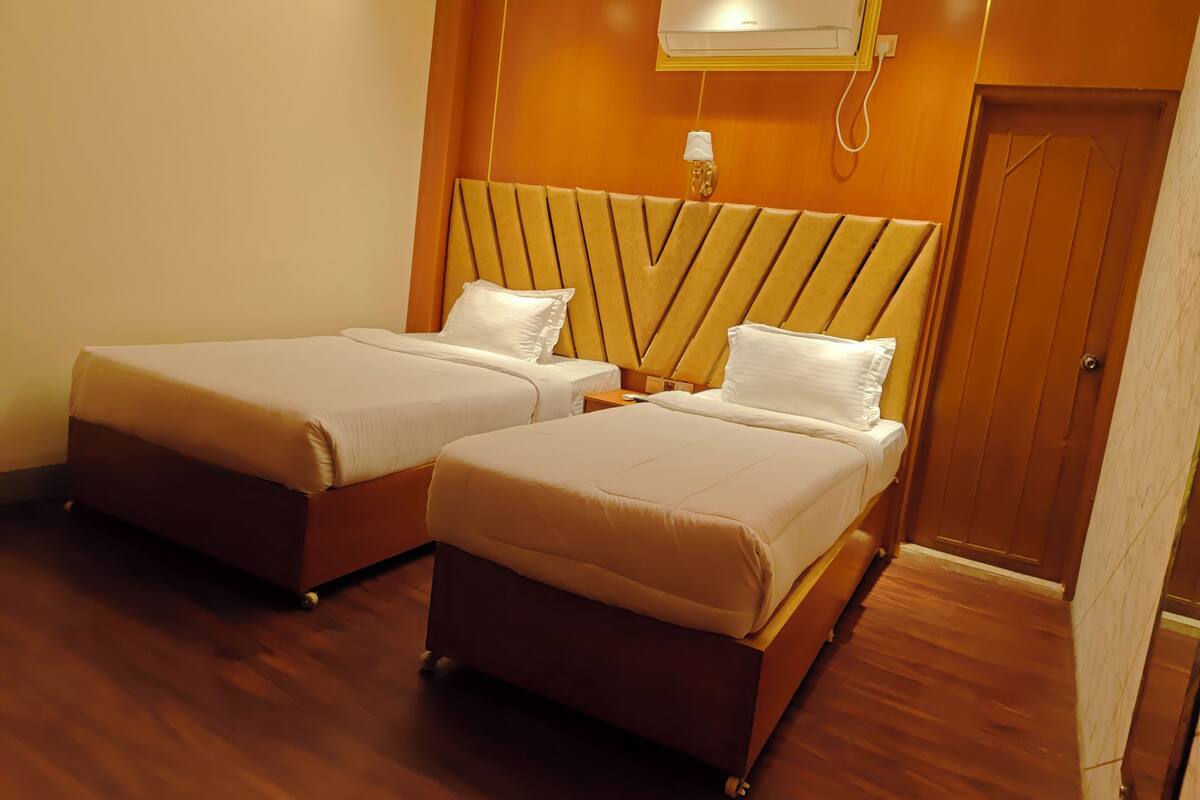 A hotel room with two beds, a wooden headboard, an air conditioning unit, and a wooden floor.