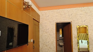Una camera d'albergo con una toeletta in legno, un televisore a schermo piatto, uno specchio con cornice decorata e un bagno piastrellato visibile attraverso una porta aperta.
