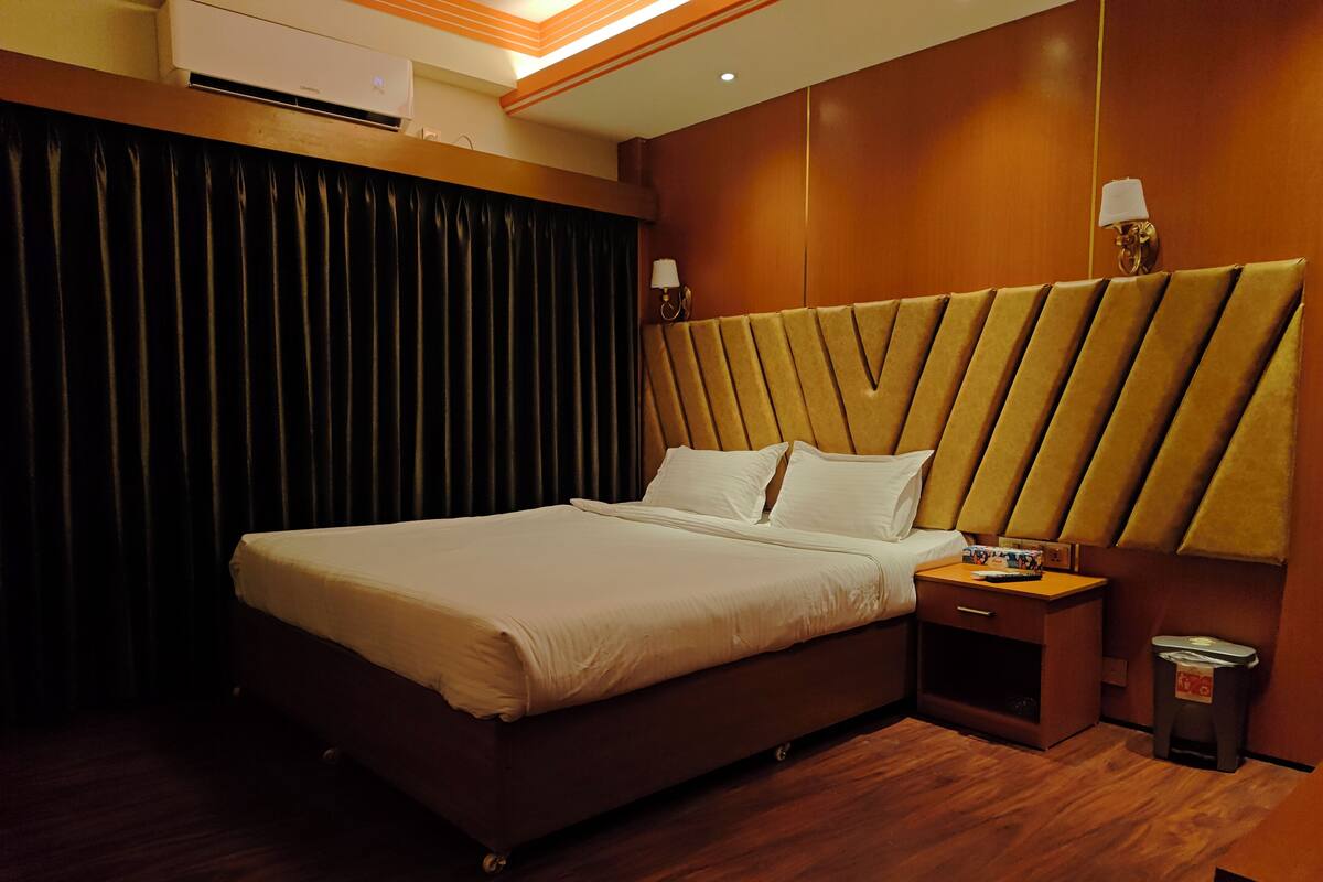 A hotel room with a bed, a nightstand, a trash bin, and a wall-mounted air conditioner.