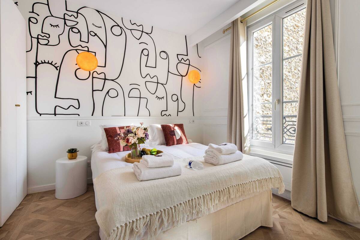Quarto de hotel moderno com uma cama grande, uma obra de arte na parede e uma janela com cortinas.