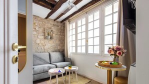Una sala de estar acogedora con una pared de piedra, un sofá gris, dos mesitas y una ventana con cortinas.