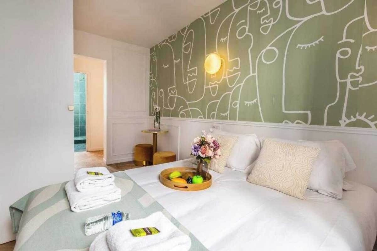 Quarto de hotel com cama, mesa de cabeceira, parede com arte abstrata e janela.