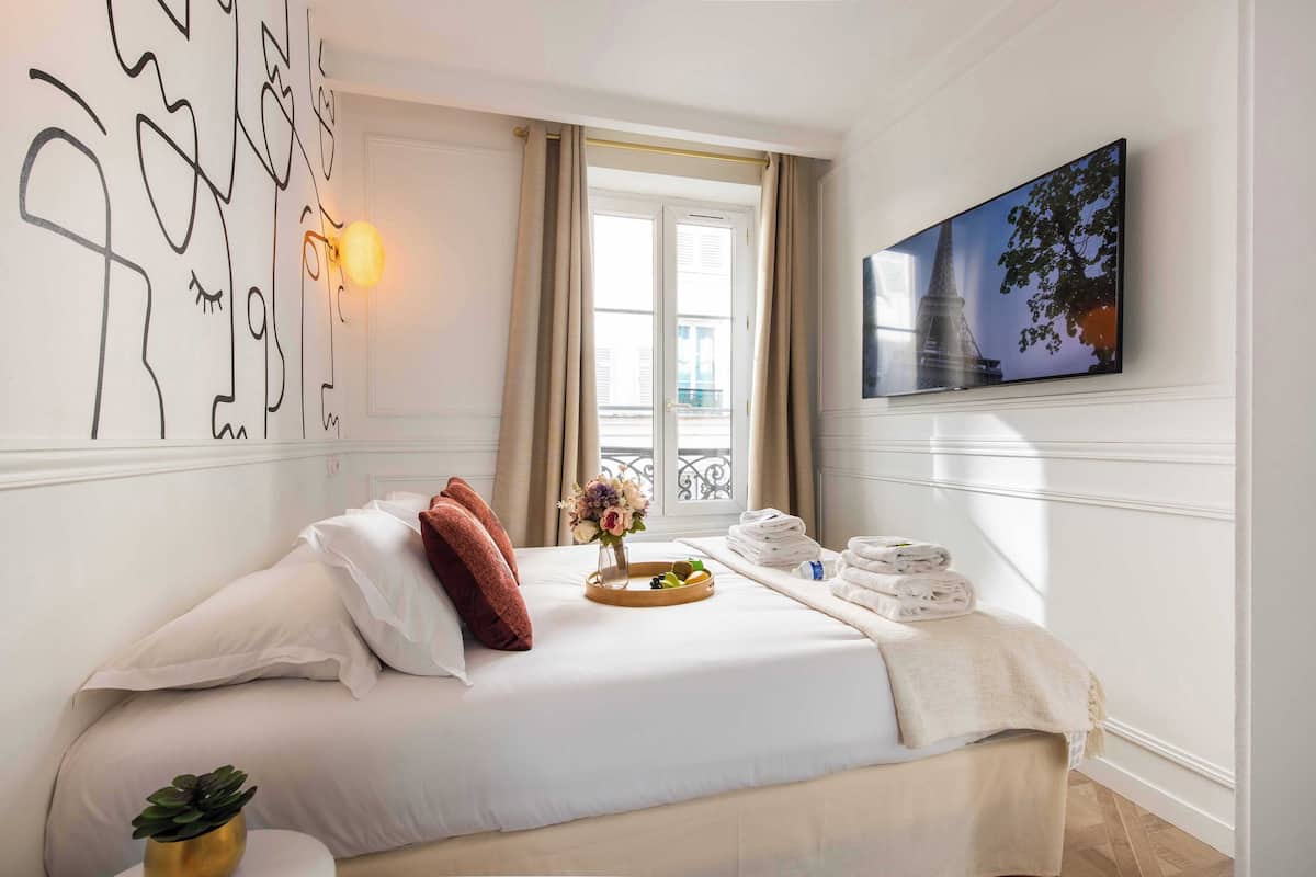 Quarto de hotel com uma cama, um vaso com flores, um porta-toalhas e um quadro na parede.