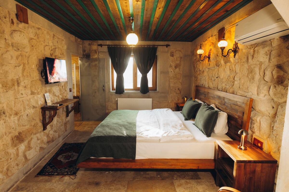 Une chambre confortable avec un mur en pierre, un cadre de lit en bois, une table de chevet avec une lampe et un téléviseur fixé au mur.