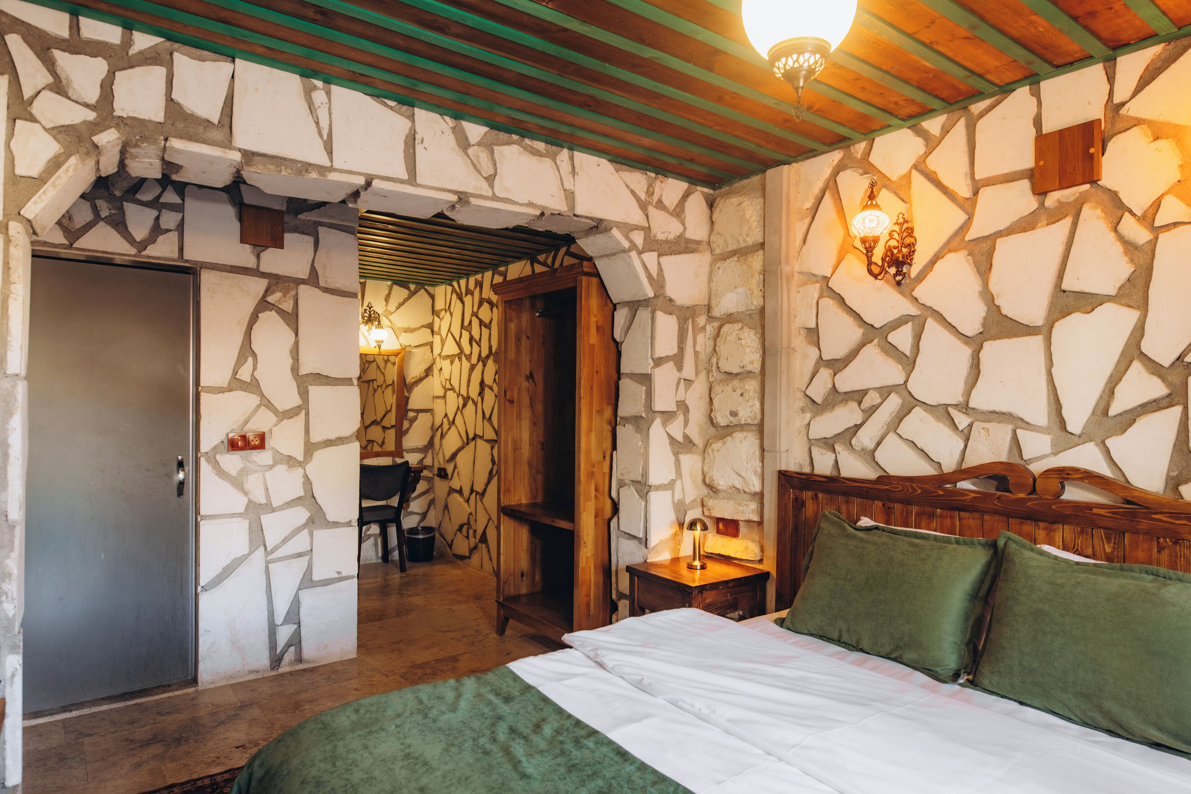 Ein Zimmer mit einer Steinsturz, einem Bett mit grünen Kissen, einem Holzkopfende und einem kleinen Tisch mit einer Lampe.